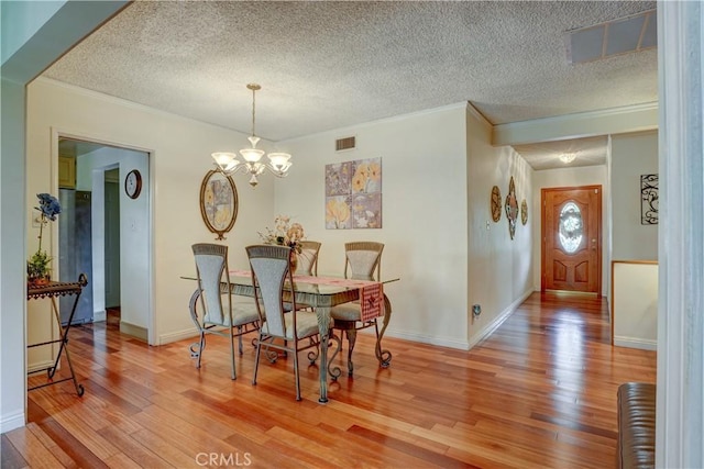 dining area with crown molding, wood-type flooring, a textured ceiling, and an inviting chandelier