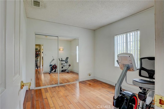 exercise room with baseboards, a textured ceiling, visible vents, and light wood-type flooring