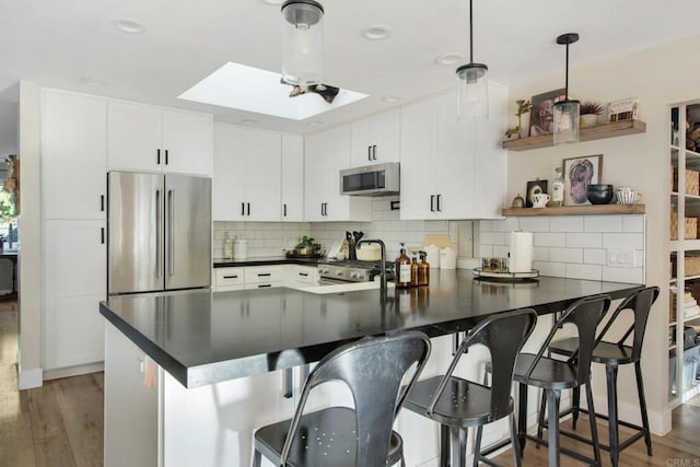 kitchen featuring white cabinets, kitchen peninsula, a breakfast bar area, a skylight, and appliances with stainless steel finishes