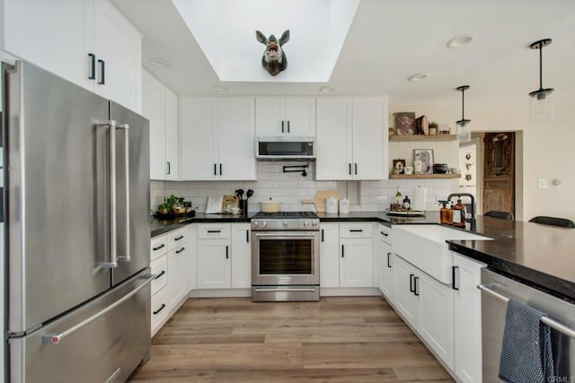 kitchen with sink, decorative light fixtures, white cabinetry, high end appliances, and backsplash