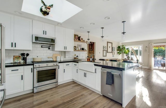 kitchen featuring appliances with stainless steel finishes, hanging light fixtures, a skylight, white cabinets, and backsplash