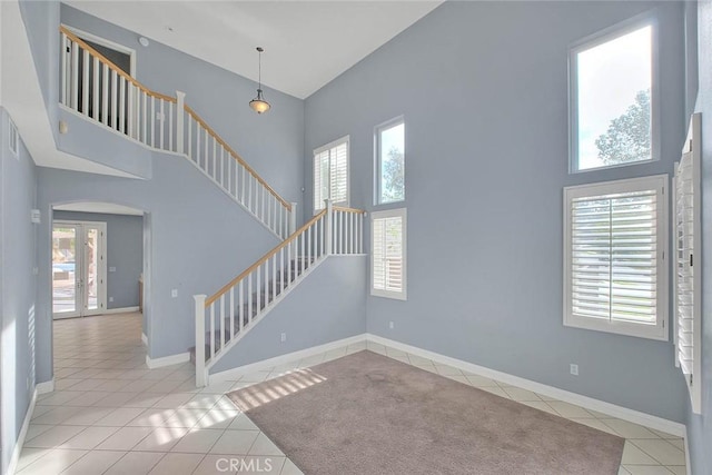 interior space with plenty of natural light, light tile patterned flooring, a towering ceiling, and french doors