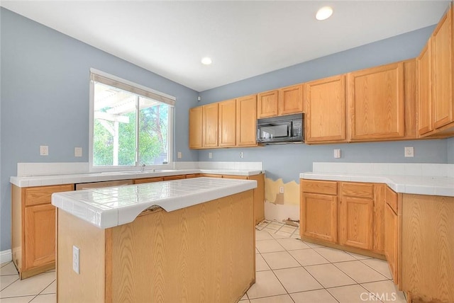 kitchen featuring a center island, light brown cabinets, stainless steel dishwasher, tile countertops, and light tile patterned flooring