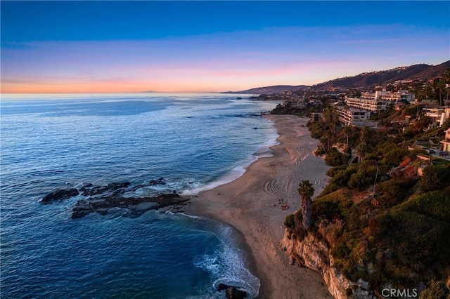 aerial view at dusk featuring a water view and a beach view