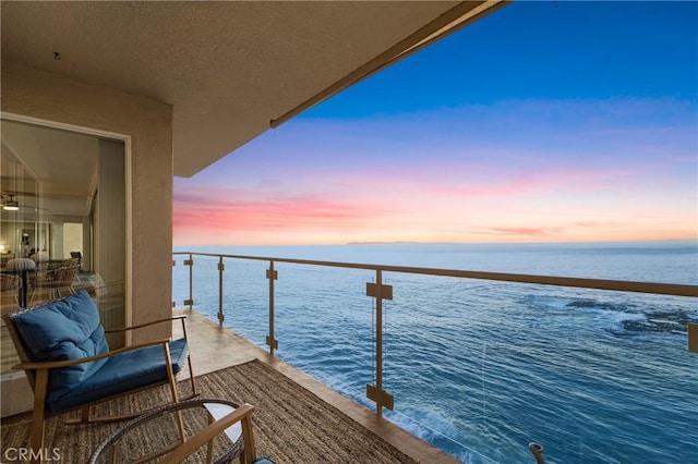 balcony at dusk featuring a water view