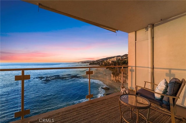 balcony at dusk featuring a water view