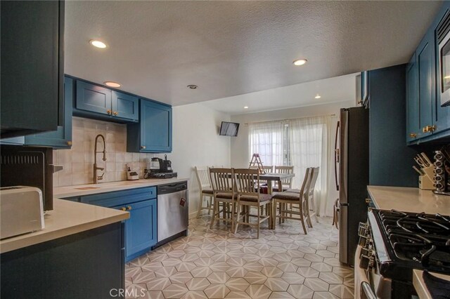 kitchen featuring sink, decorative backsplash, blue cabinetry, a textured ceiling, and stainless steel appliances