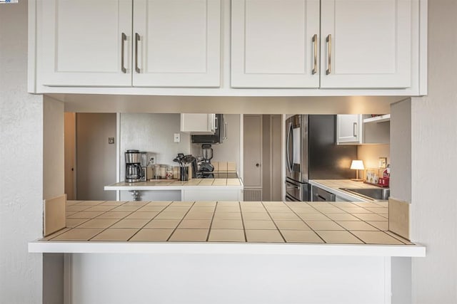 kitchen featuring tile counters, white cabinetry, sink, and stainless steel refrigerator