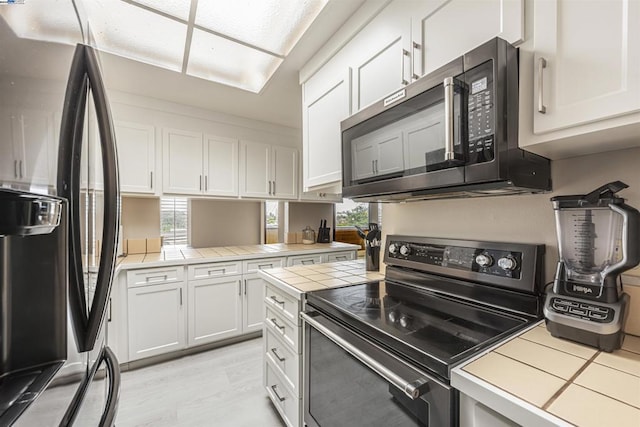 kitchen with black appliances, white cabinets, and tile countertops