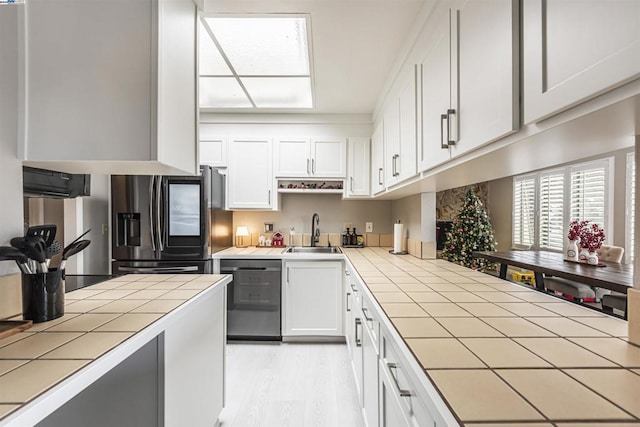 kitchen with light wood-type flooring, stainless steel appliances, sink, tile countertops, and white cabinetry