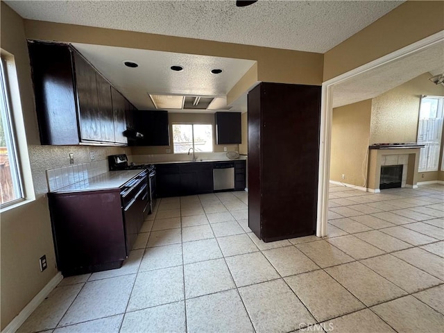 kitchen with a tile fireplace, sink, a textured ceiling, stainless steel appliances, and light tile patterned floors