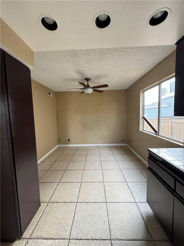 interior space featuring ceiling fan, light tile patterned flooring, and a textured ceiling