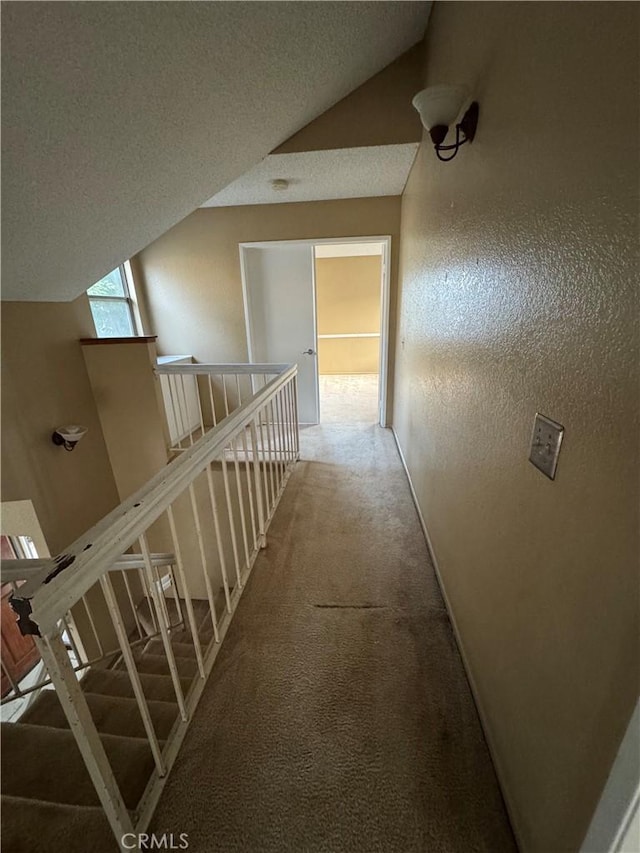 corridor with a textured ceiling, lofted ceiling, and carpet floors