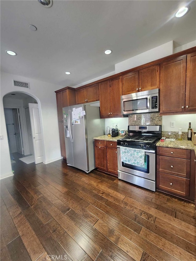 kitchen featuring decorative backsplash, light stone countertops, dark wood-type flooring, and appliances with stainless steel finishes