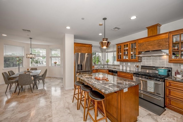 kitchen featuring a center island, dark stone countertops, extractor fan, decorative light fixtures, and appliances with stainless steel finishes