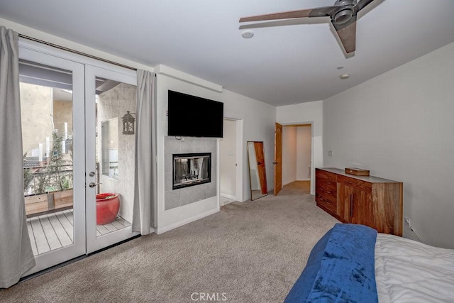 carpeted bedroom featuring access to exterior, ceiling fan, and a tiled fireplace