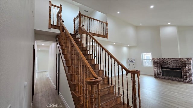 stairs featuring hardwood / wood-style flooring, a high ceiling, and a brick fireplace