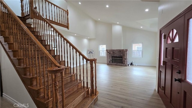 entryway with light hardwood / wood-style flooring, high vaulted ceiling, and a brick fireplace