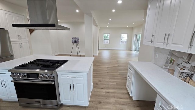 kitchen with light stone counters, island exhaust hood, appliances with stainless steel finishes, white cabinets, and light wood-type flooring