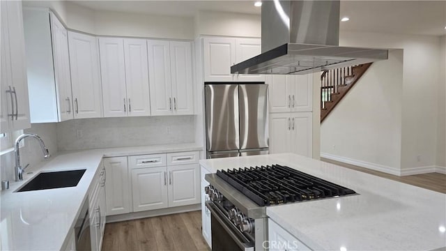 kitchen with wall chimney exhaust hood, stainless steel appliances, sink, light hardwood / wood-style flooring, and white cabinetry