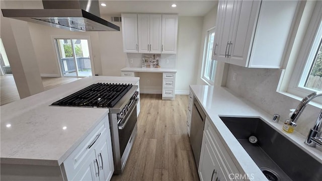 kitchen featuring appliances with stainless steel finishes, sink, wall chimney range hood, white cabinets, and light hardwood / wood-style floors