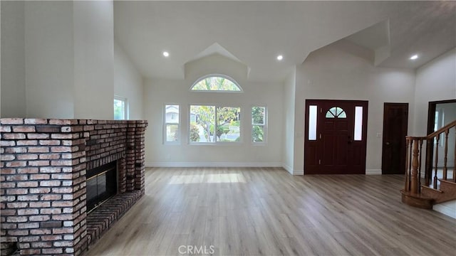 foyer entrance featuring a fireplace, light hardwood / wood-style flooring, and high vaulted ceiling