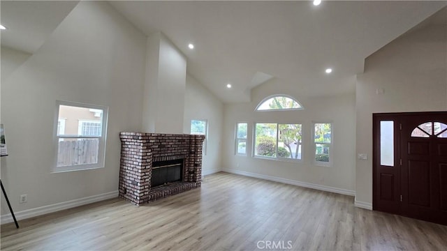 unfurnished living room featuring a brick fireplace, high vaulted ceiling, and light hardwood / wood-style flooring