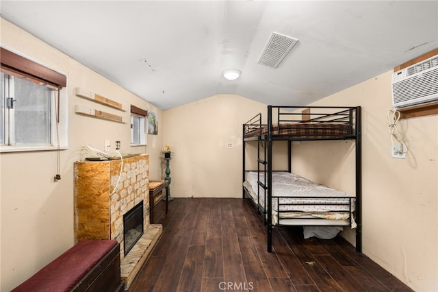 bedroom featuring a wall unit AC, a stone fireplace, dark hardwood / wood-style floors, and vaulted ceiling