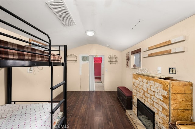 bedroom with hardwood / wood-style floors, a stone fireplace, and lofted ceiling