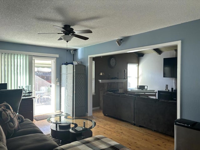 living room featuring ceiling fan, hardwood / wood-style floors, a tile fireplace, and a textured ceiling