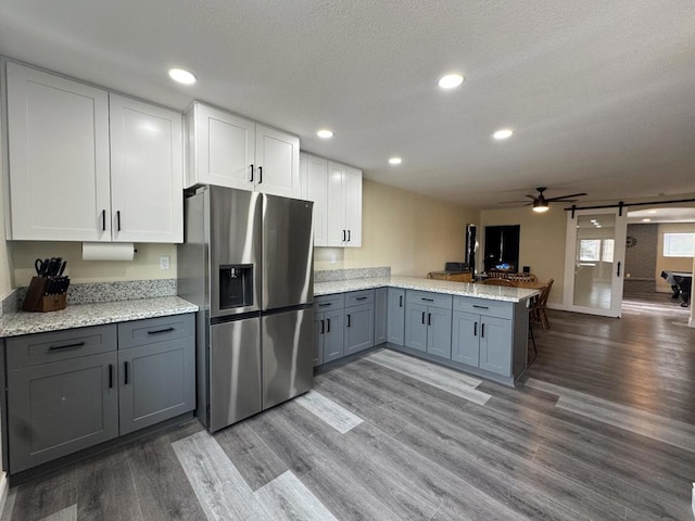 kitchen featuring a barn door, kitchen peninsula, hardwood / wood-style flooring, stainless steel fridge with ice dispenser, and white cabinets