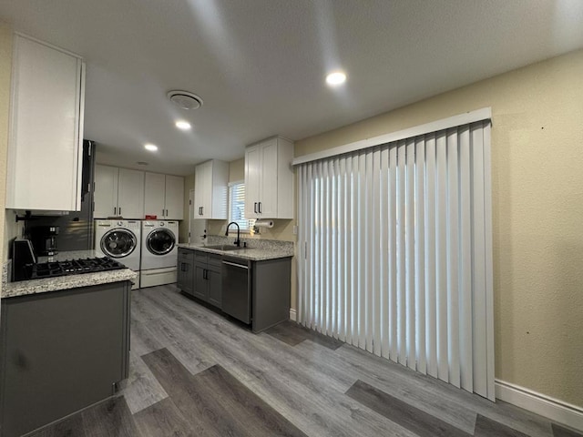 kitchen with hardwood / wood-style floors, appliances with stainless steel finishes, washing machine and dryer, white cabinetry, and sink