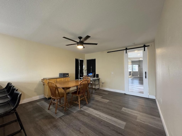 dining space with ceiling fan, dark wood-type flooring, a textured ceiling, and a barn door