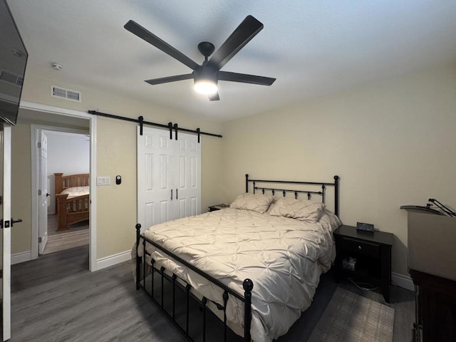 bedroom featuring ceiling fan, a barn door, a closet, and dark wood-type flooring