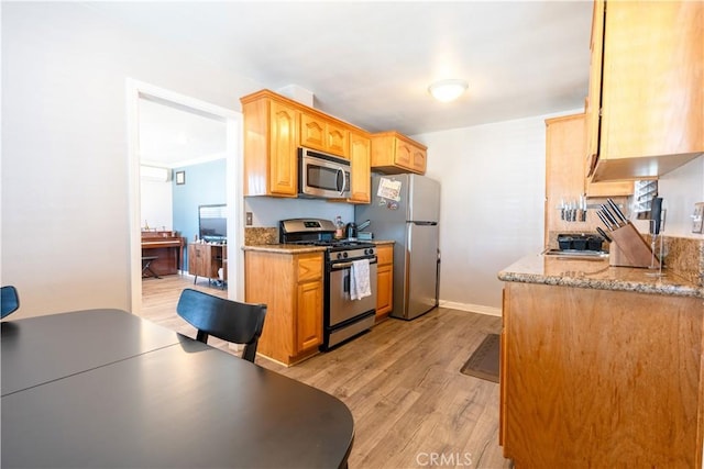 kitchen with light stone countertops, stainless steel appliances, and light hardwood / wood-style flooring