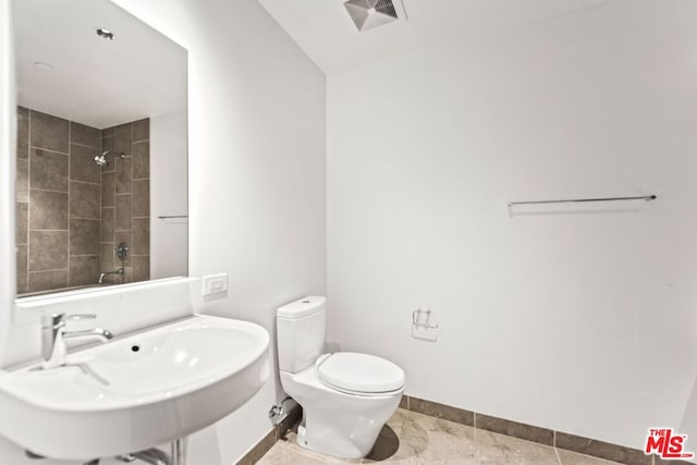 bathroom featuring a tile shower, toilet, tile patterned floors, and sink