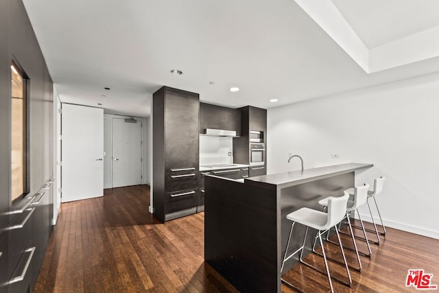 kitchen featuring a breakfast bar, sink, dark hardwood / wood-style floors, appliances with stainless steel finishes, and kitchen peninsula