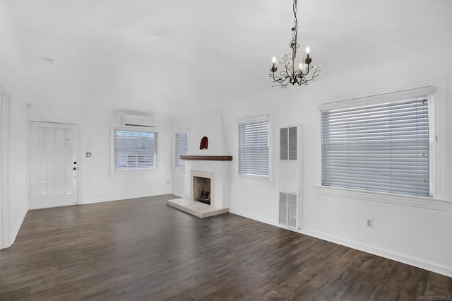 unfurnished living room with a chandelier, a wall mounted AC, and dark wood-type flooring