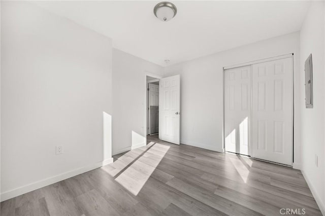 unfurnished bedroom featuring electric panel, light hardwood / wood-style floors, and a closet