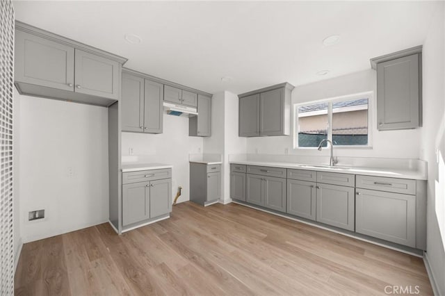 kitchen with light wood-type flooring, gray cabinets, and sink