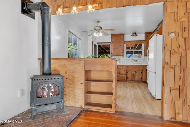 kitchen featuring tasteful backsplash, ceiling fan, wood-type flooring, white refrigerator, and a wood stove