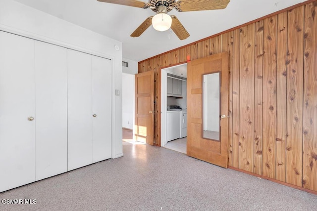 unfurnished bedroom featuring ceiling fan, wood walls, separate washer and dryer, and a closet