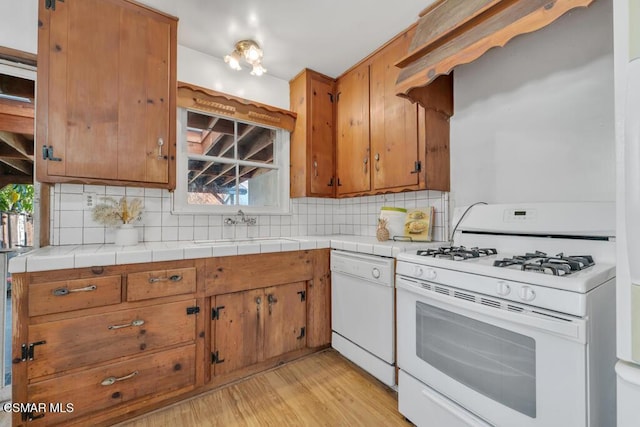 kitchen featuring sink, tasteful backsplash, tile countertops, white appliances, and light wood-type flooring