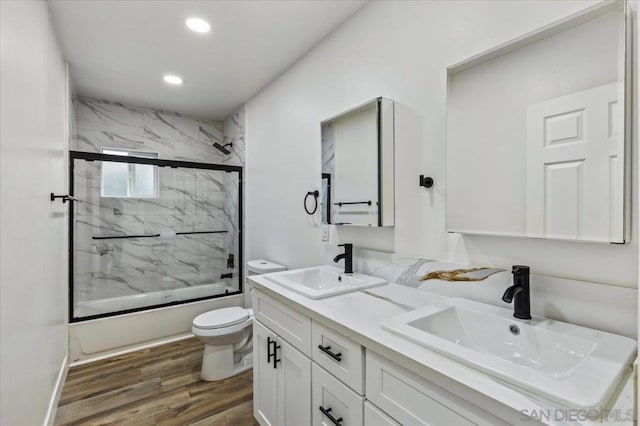 full bathroom featuring hardwood / wood-style floors, vanity, toilet, and bath / shower combo with glass door