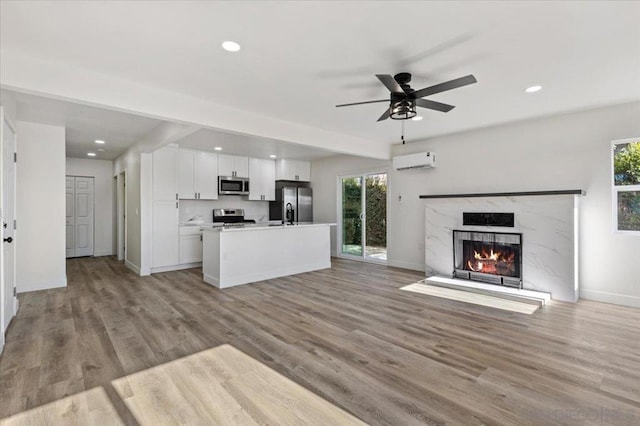 unfurnished living room with a wall mounted AC, ceiling fan, beamed ceiling, a fireplace, and light hardwood / wood-style floors