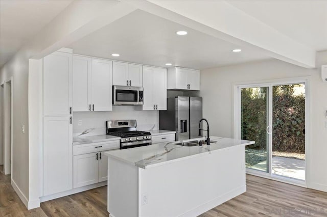 kitchen with light wood-type flooring, stainless steel appliances, sink, a center island with sink, and white cabinetry