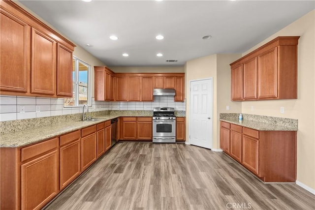 kitchen with light stone counters, sink, light hardwood / wood-style floors, and appliances with stainless steel finishes