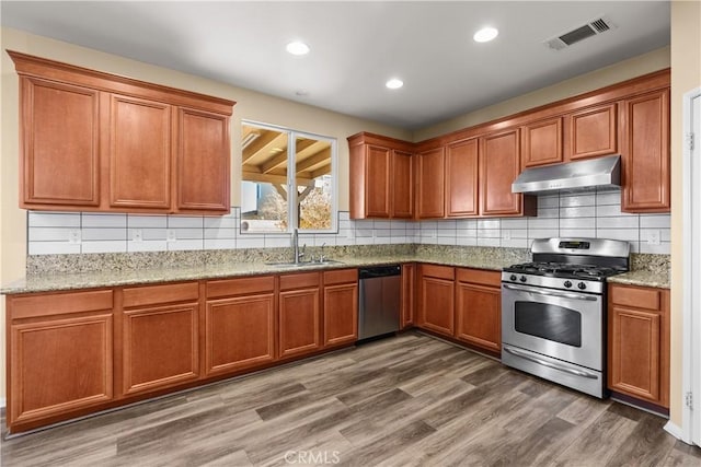 kitchen with appliances with stainless steel finishes, backsplash, light stone counters, sink, and dark hardwood / wood-style floors