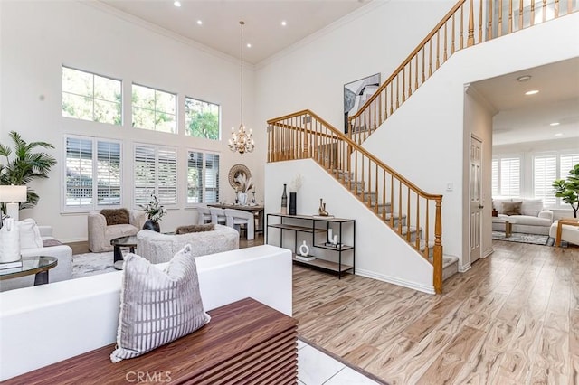 living room with a towering ceiling, light hardwood / wood-style floors, crown molding, and a notable chandelier