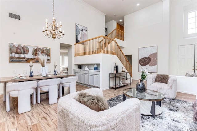 living room with light wood-type flooring, crown molding, a high ceiling, and a chandelier